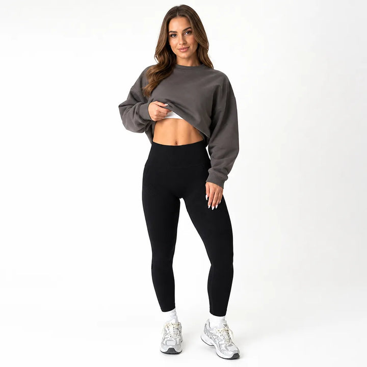 Femme de face en legging noir taille haute, sweat court gris relevé sur le ventre, baskets claires. 5