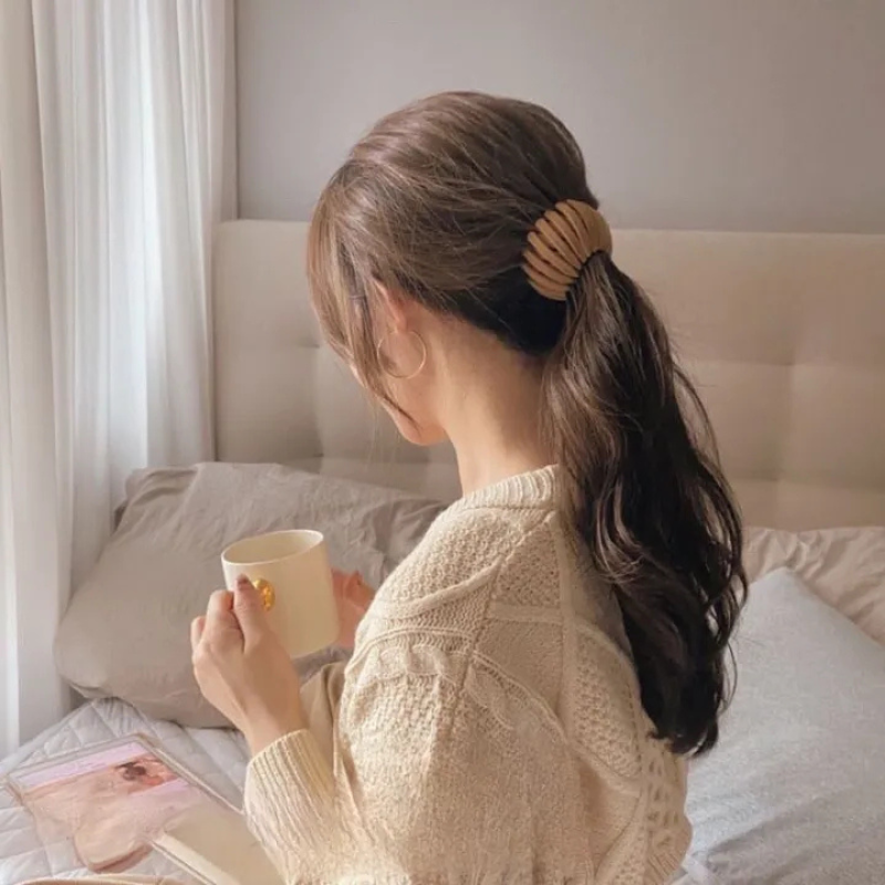 Femme de dos assise sur un lit, tasse à la main, cheveux mi-attachés par une pince beige à lamelles. 2