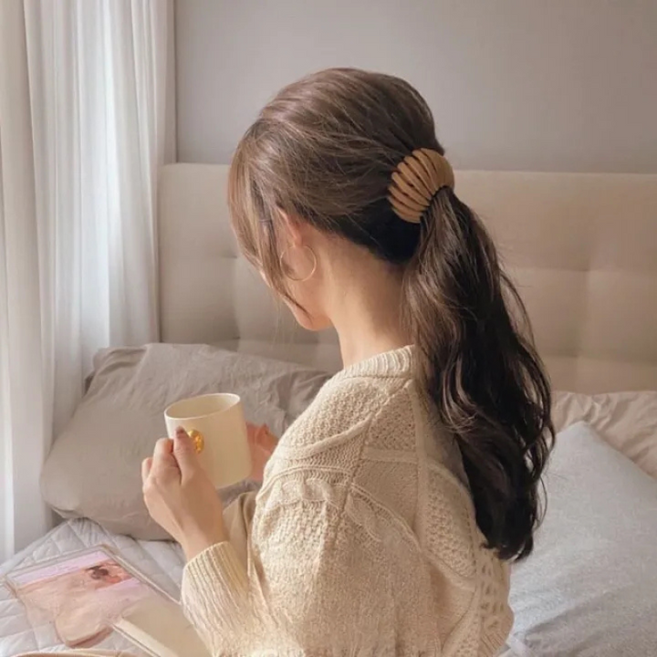 Femme de dos assise sur un lit, tasse à la main, cheveux mi-attachés par une pince beige à lamelles. 2