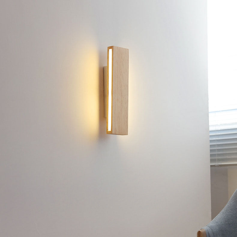 Applique en bois verticale allumée sur un mur blanc, dans une pièce avec store à lamelles et fauteuil gris. 15