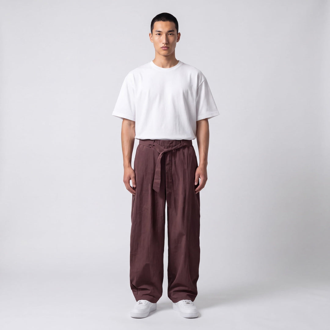 Mannequin de face en pied portant le pantalon large marron prune, ceinture nouée à la taille, avec t-shirt blanc et baskets blanches. 7
