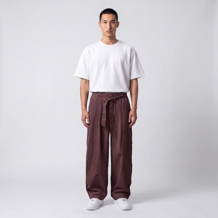 Mannequin de face en pied portant le pantalon large marron prune, ceinture nouée à la taille, avec t-shirt blanc et baskets blanches. 7