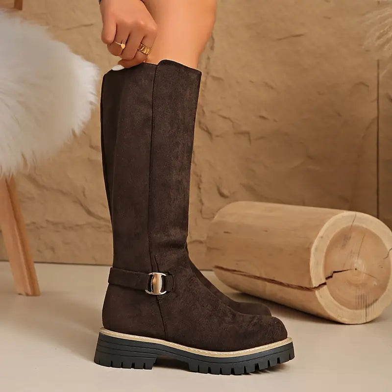 Botte marron foncé portée de profil, jambe tendue, avec sangle à boucle dorée et semelle épaisse à crampons. 7