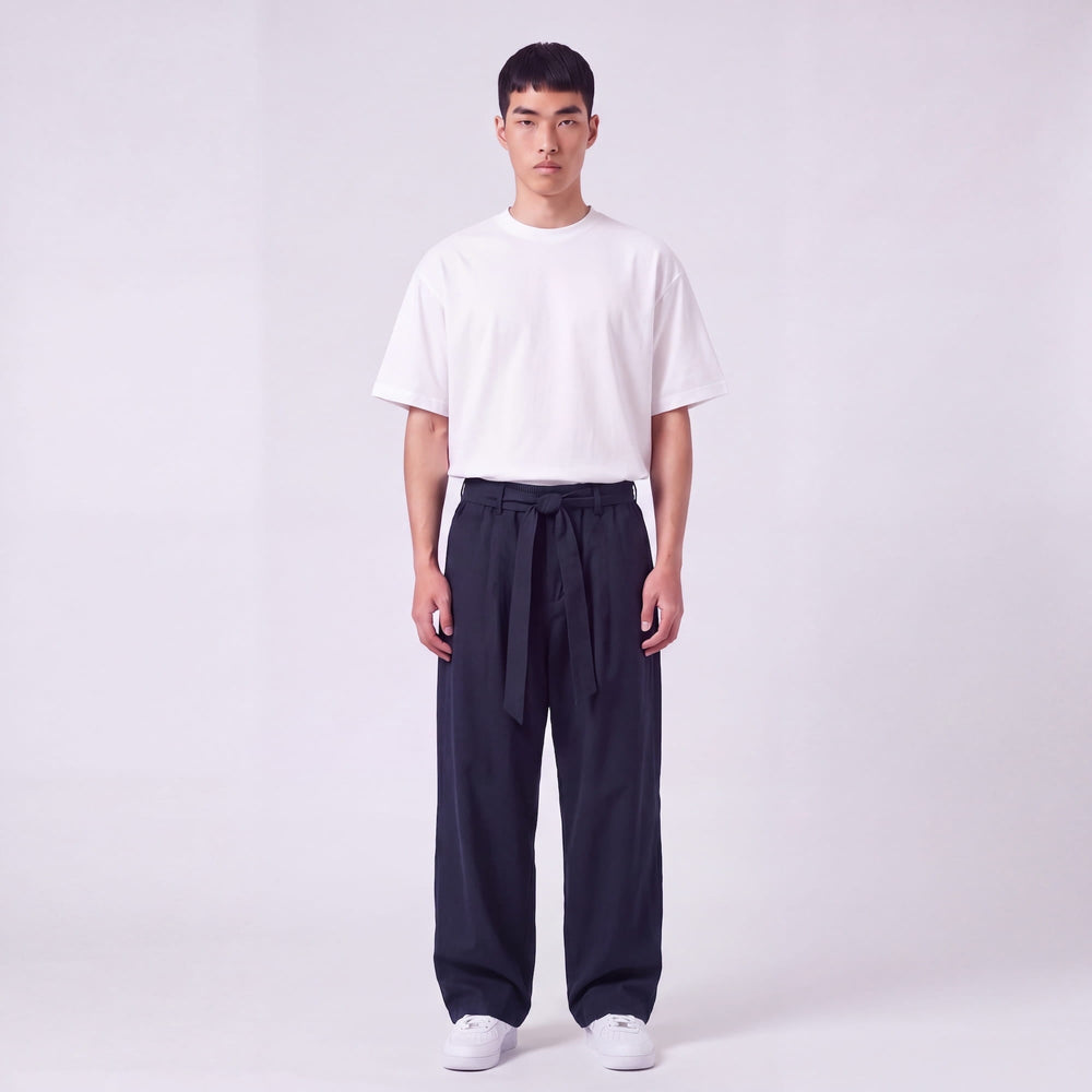 Mannequin de face en pied portant le pantalon large bleu marine, ceinture nouée à la taille, avec t-shirt blanc oversize. 2