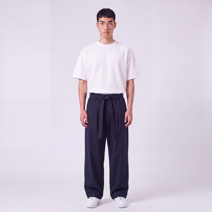 Mannequin de face en pied portant le pantalon large bleu marine, ceinture nouée à la taille, avec t-shirt blanc oversize. 2