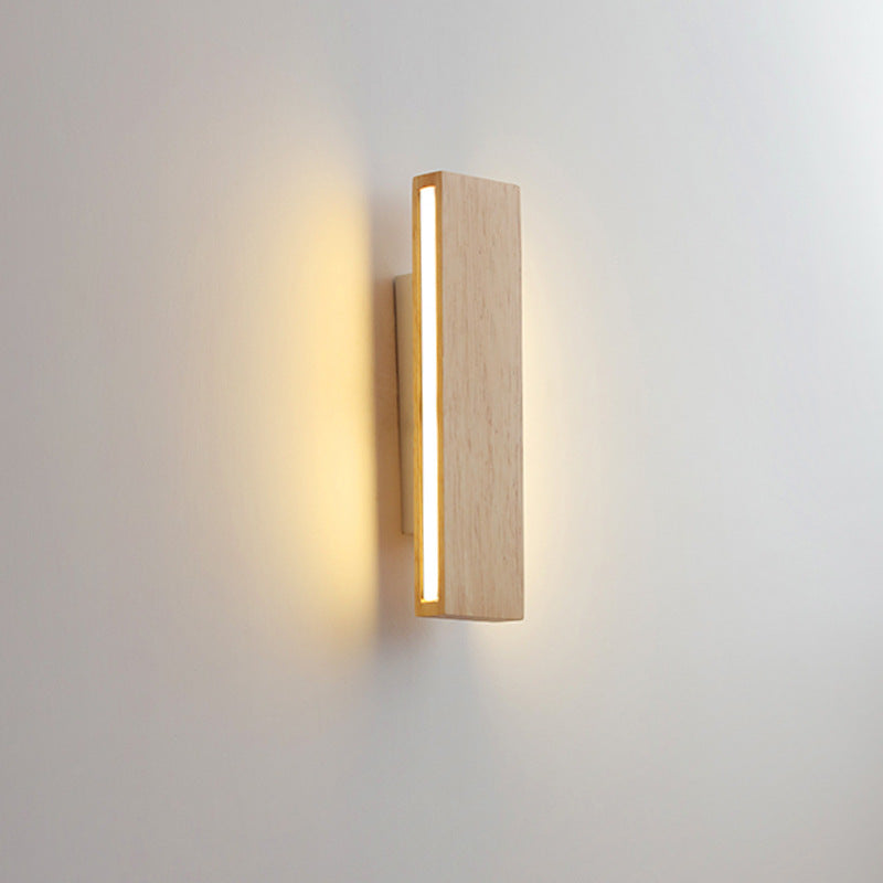 Applique en bois en position verticale, allumée, avec une fine bande lumineuse sur le côté et un halo chaud sur le mur. 10