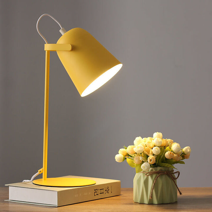 Lampe jaune allumée posée sur un livre, avec un petit vase vert et un bouquet de roses blanches à côté. 1