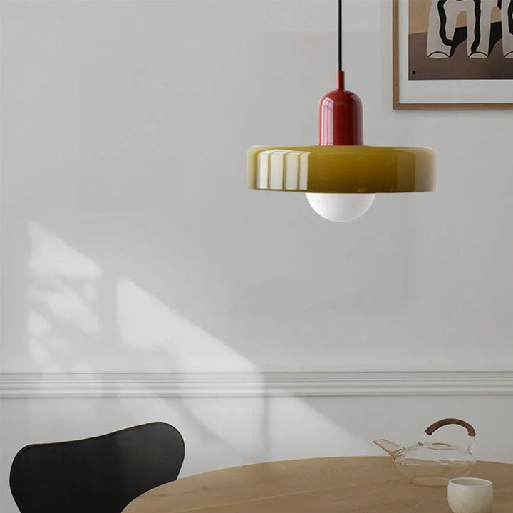 Suspension à verre vert olive et capuchon rouge bordeaux, installée au-dessus d'une table en bois dans une salle à manger lumineuse. 25