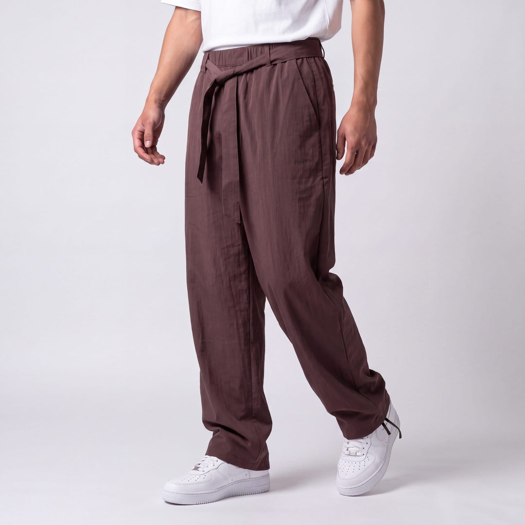 Vue de trois quarts du pantalon marron prune en marche, montrant la ceinture nouée, la poche latérale et la cheville resserrée. 8