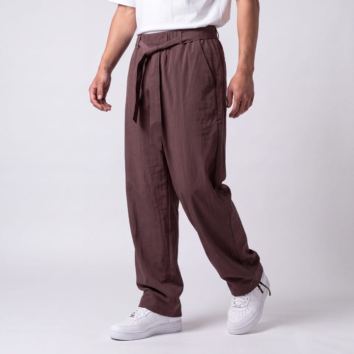 Vue de trois quarts du pantalon marron prune en marche, montrant la ceinture nouée, la poche latérale et la cheville resserrée. 8
