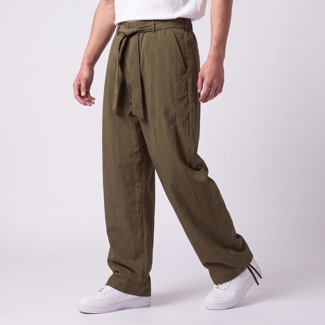 Vue de trois quarts du pantalon vert kaki en marche, avec ceinture à nouer, poche latérale et cordon de cheville. 10