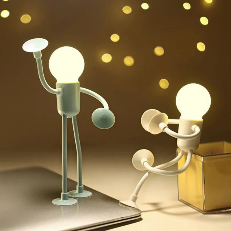 Deux veilleuses allumées, l'une verte debout sur un ordinateur portable, l'autre blanche adossée à un cube transparent, lumières floues en fond. 8