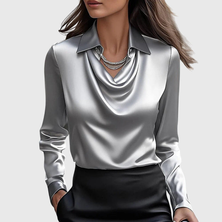 Blouse en satin gris argenté à col drapé et manches longues, portée avec une jupe noire et un collier de strass. 2