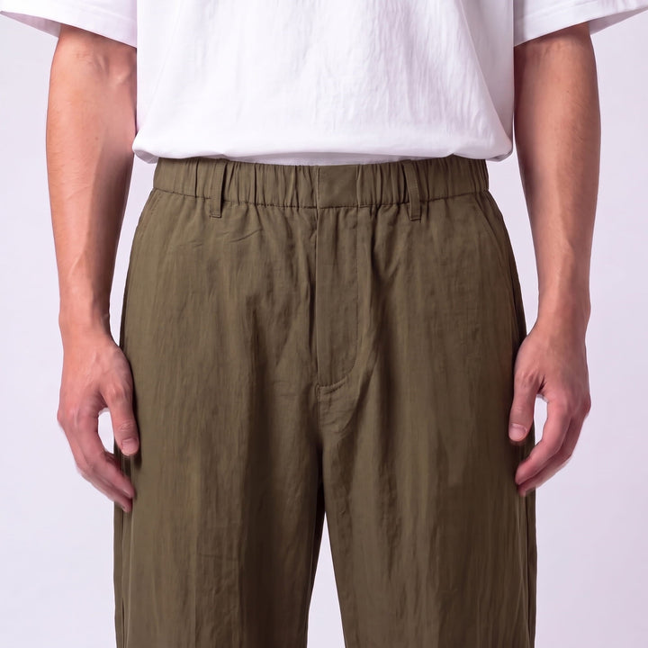 Gros plan de face sur la taille élastique, les passants et la fermeture du pantalon vert kaki, tissu froissé. 11