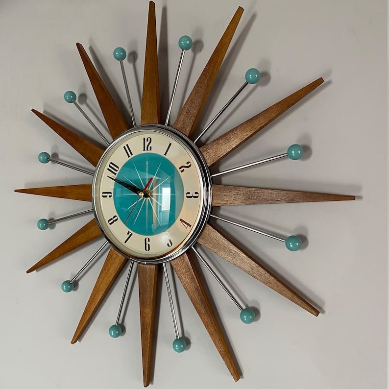 Horloge en étoile vue légèrement de biais sur un mur gris, montrant l'ombre portée des rayons en bois et des tiges chromées. 3