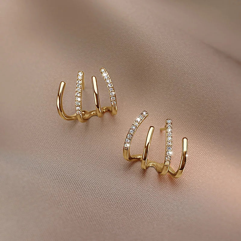 Paire de boucles dorées à quatre griffes dont deux serties de strass, posée sur un tissu rosé 9