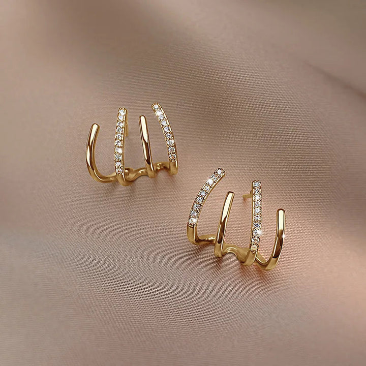 Paire de boucles dorées à quatre griffes dont deux serties de strass, posée sur un tissu rosé 9