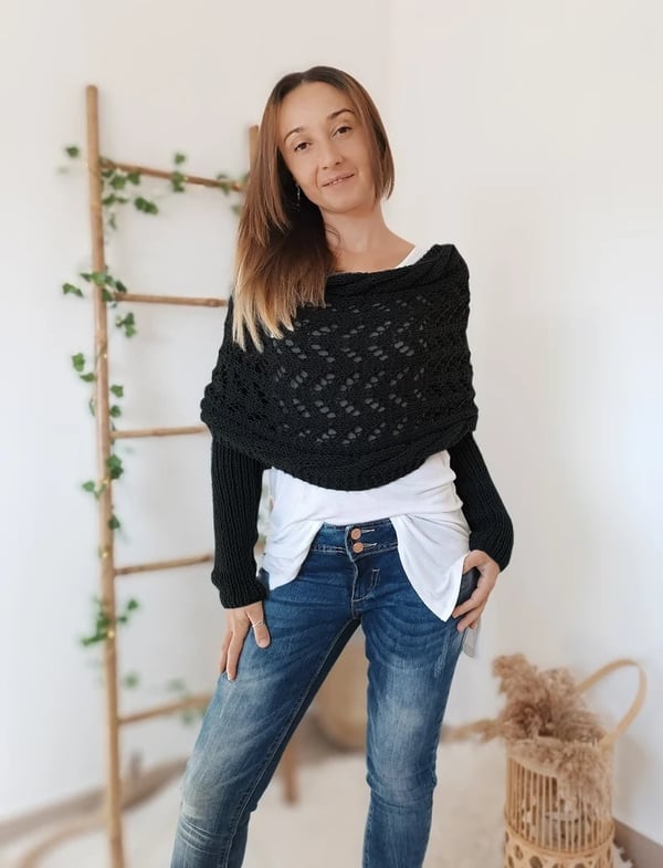 Châle noir en maille ajourée à manches intégrées, porté de face sur un t-shirt blanc et un jean, mains dans les poches. 1