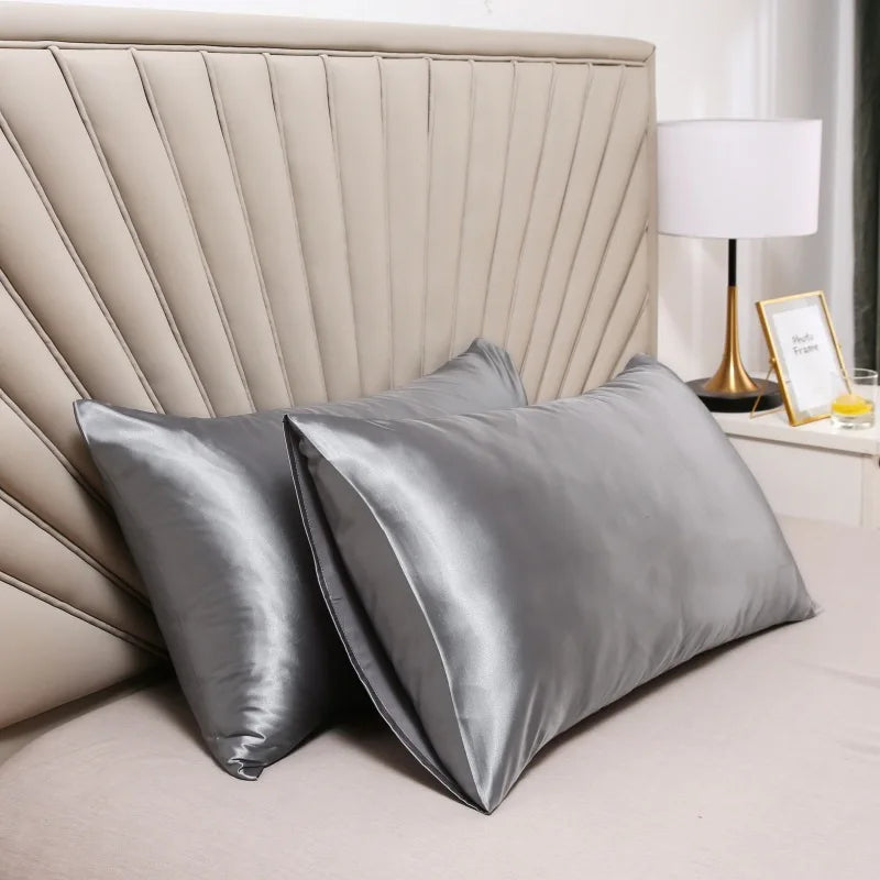 Deux taies satinées grises posées sur un lit devant une tête de lit beige et une lampe de chevet 2