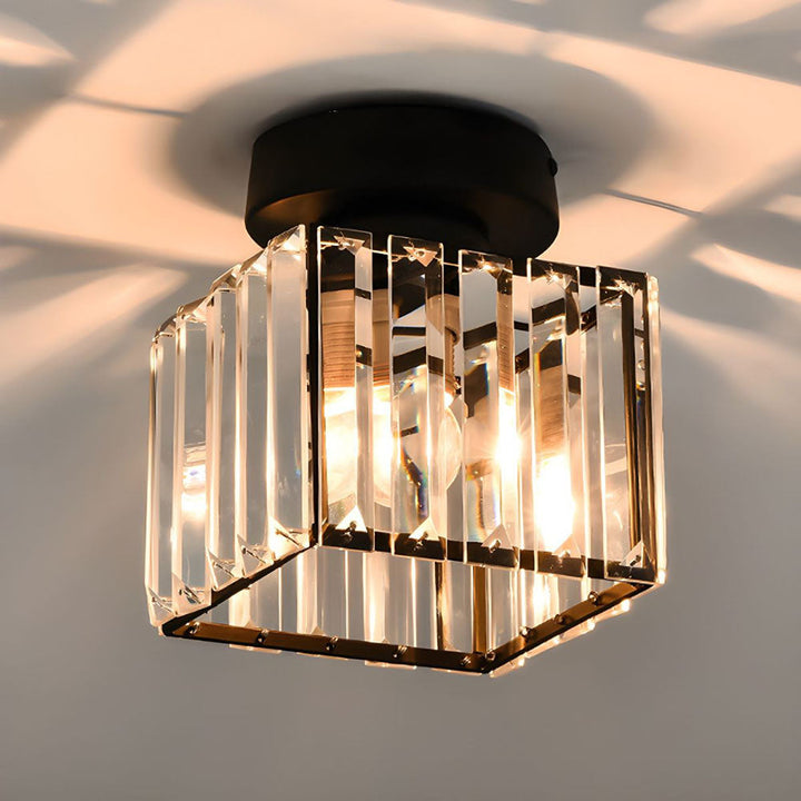 Gros plan sur le plafonnier carré à lames de cristal et base ronde noire, ampoules allumées, ombres sur le plafond. 3