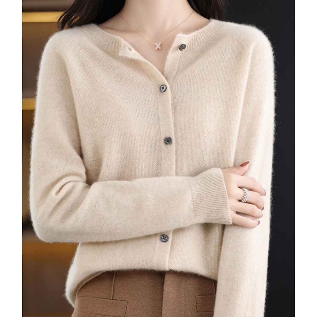 Cardigan beige clair à col rond et boutons gris, porté avec un pantalon marron, bras replié sur le buste. 15