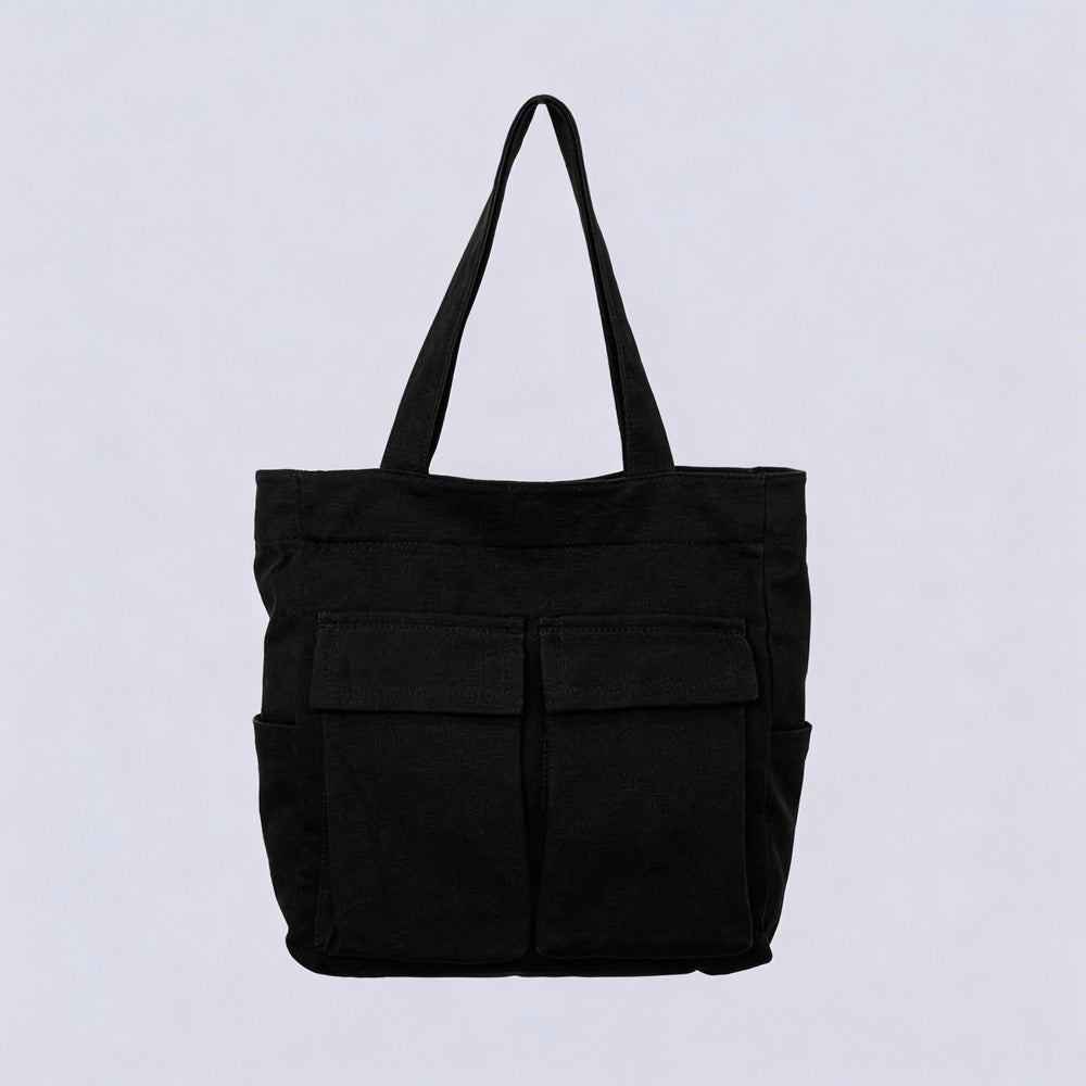 Sac cabas noir en toile, vu de face sur fond clair, avec deux grandes poches à rabat et deux poches latérales. 1