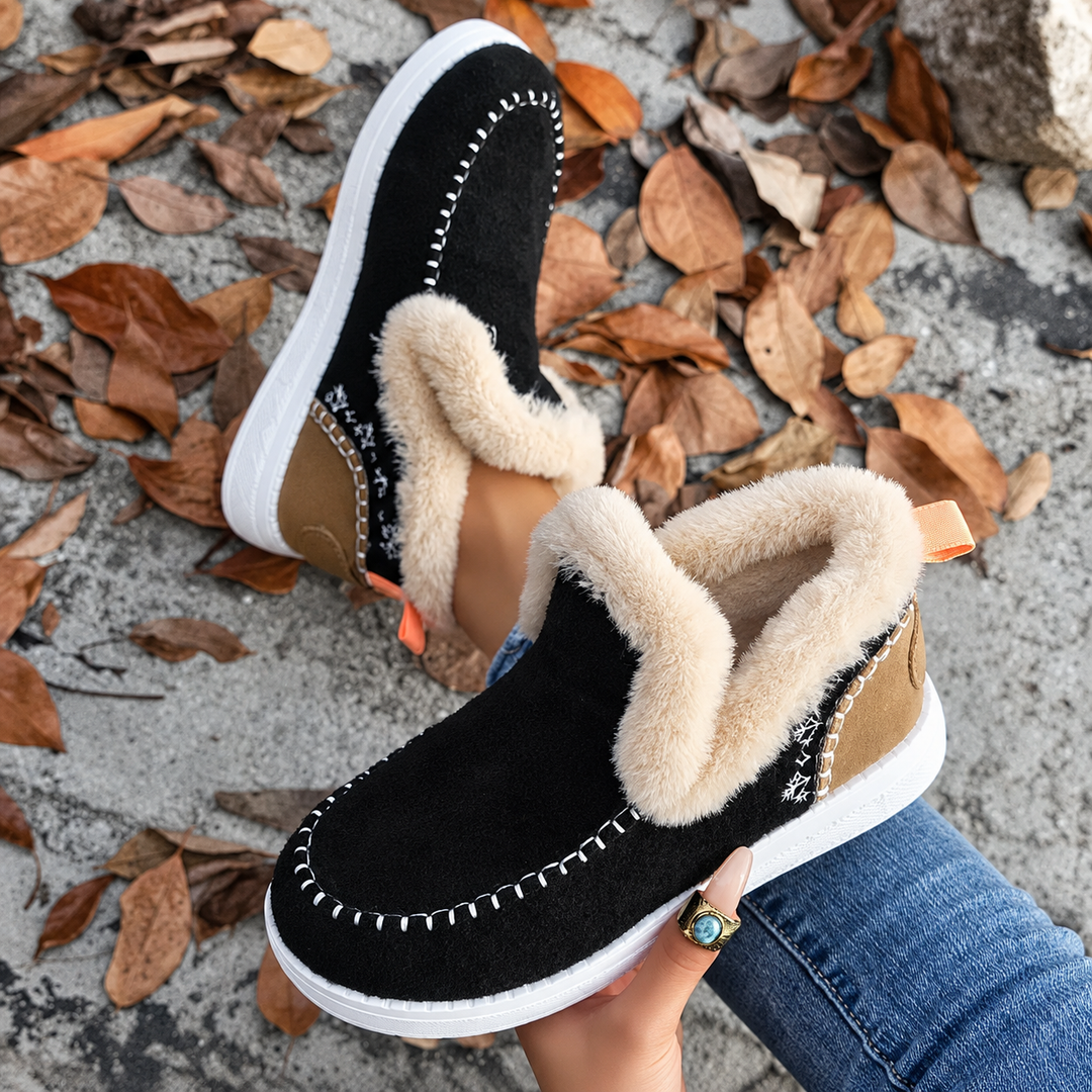 Paire noire tenue en main, vue en plongée sur la broderie de flocons, le talon fauve et la doublure en peluche. 7