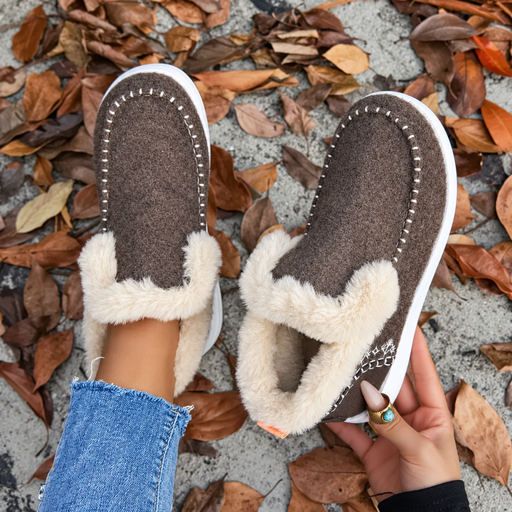 Vue de dessus de la paire marron, un pied chaussé et l'autre tenu en main pour montrer l'intérieur peluche. 8