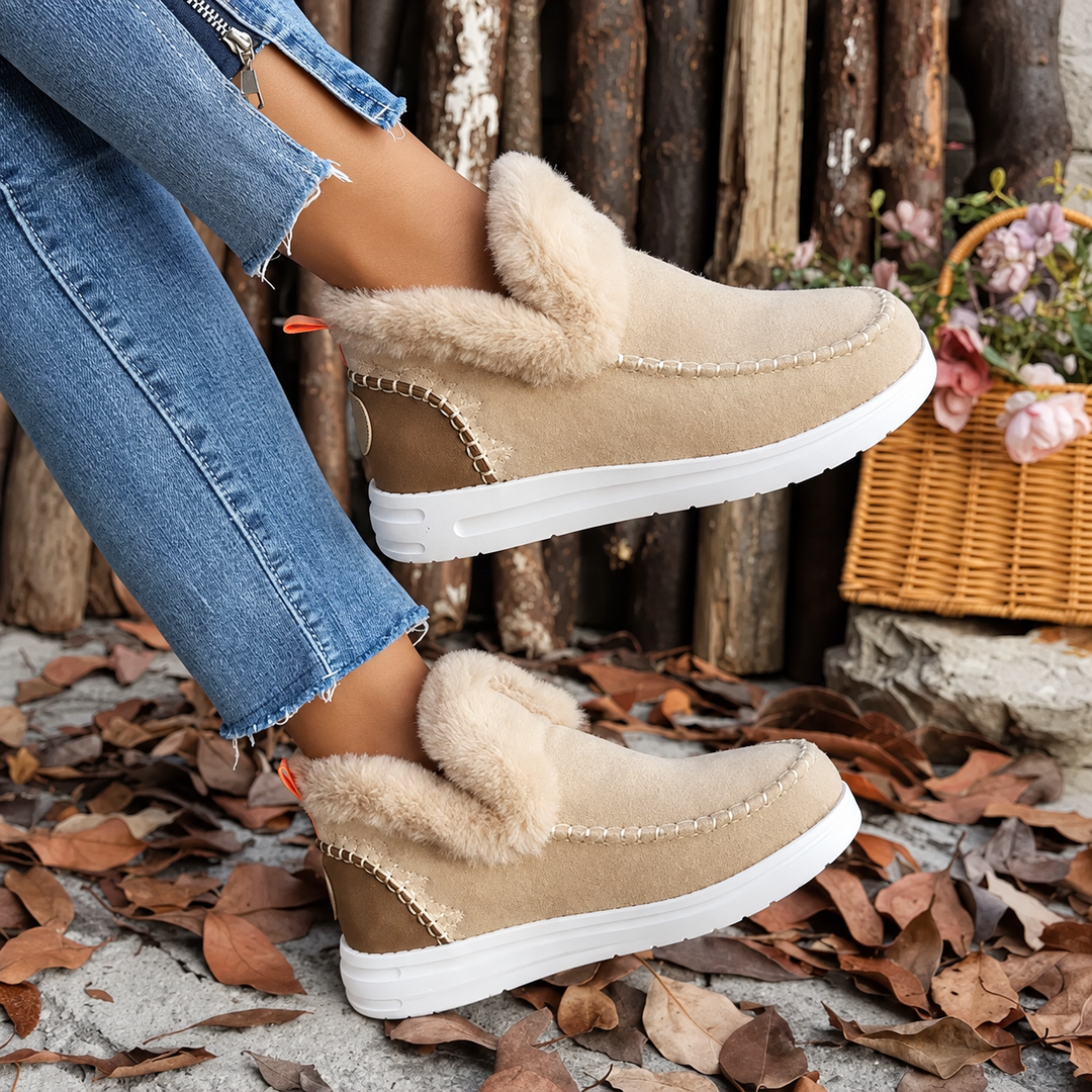 Paire beige en suédine portée, pieds croisés devant un panier d'osier, avec col en fourrure douce et couture apparente. 3