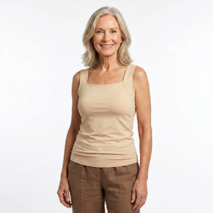 Femme aux cheveux blonds souriante, de face, portant un débardeur beige à encolure carrée et un pantalon marron. 1