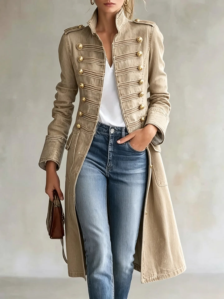 Manteau croisé à col officier en coloris beige sable, boutons dorés et galons, porté avec jean et tee-shirt blanc. 8