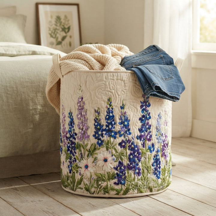 Panier brodé de fleurs bleues et violettes près d'un lit, débordant d'un plaid en maille crème et d'un jean plié. 5
