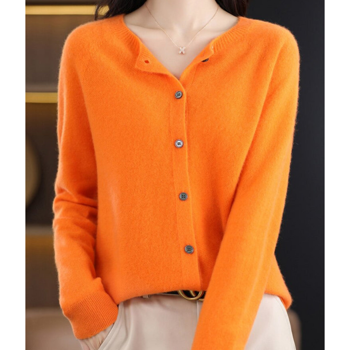 Cardigan orange vif à col rond et boutons gris, porté avec un pantalon beige et un collier à pendentif. 8