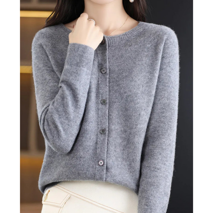 Cardigan gris chiné à col rond et boutons foncés, porté avec un pantalon crème, main posée près du col. 7
