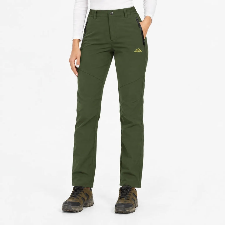 Pantalon vert foncé porté de face par une mannequin, poches zippées et chaussures de randonnée 7