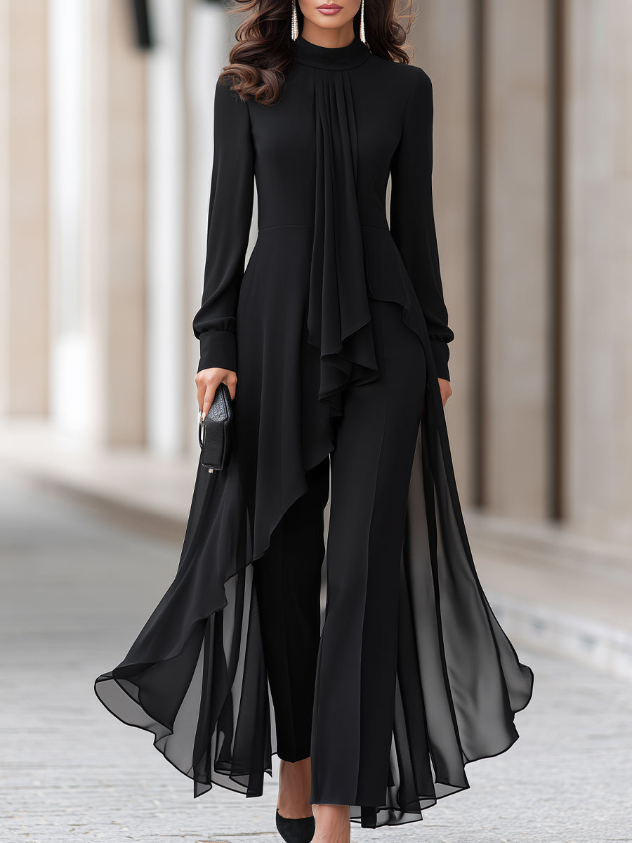 Femme en tunique noire de mousseline à col montant et pantalon large, plan rapproché cadré du cou aux chevilles, pochette noire à la main. 1