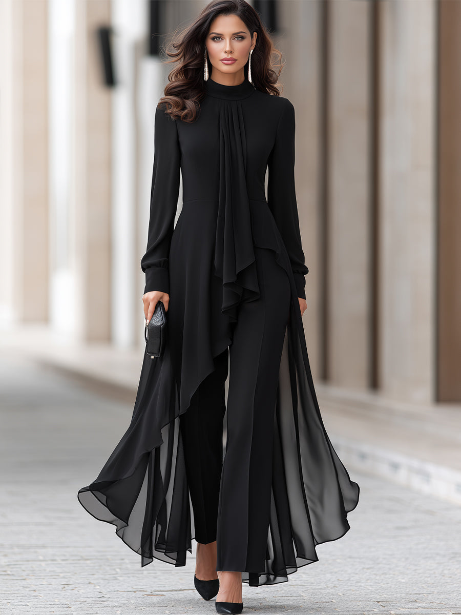 Tenue noire portée en pied par un mannequin sur une allée pavée : tunique asymétrique en mousseline, pantalon large, escarpins noirs et pochette. 2