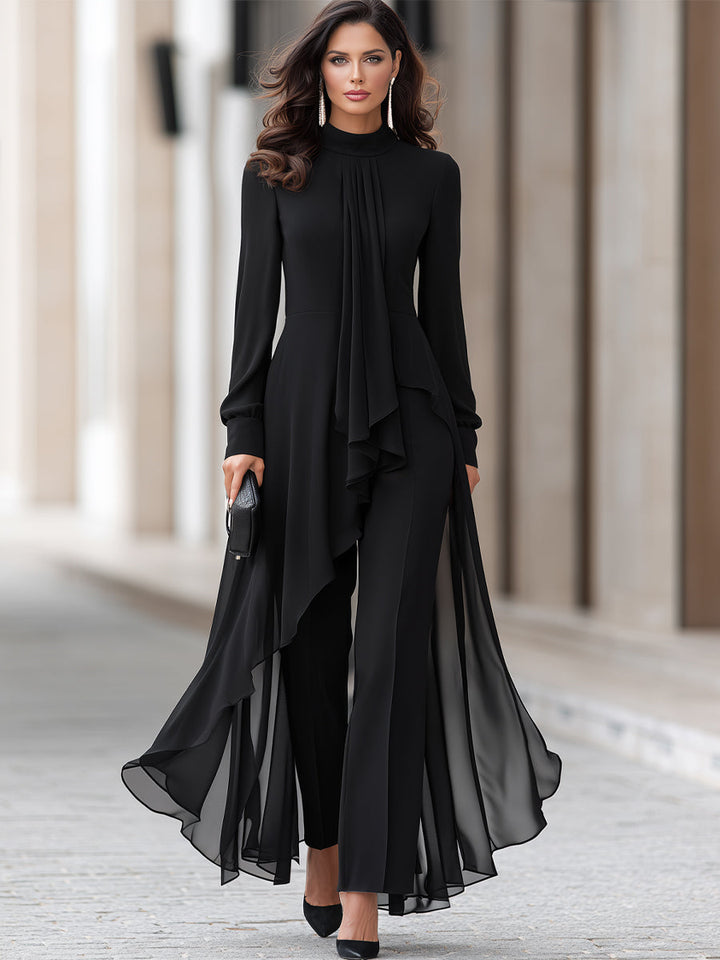 Tenue noire portée en pied par un mannequin sur une allée pavée : tunique asymétrique en mousseline, pantalon large, escarpins noirs et pochette. 2