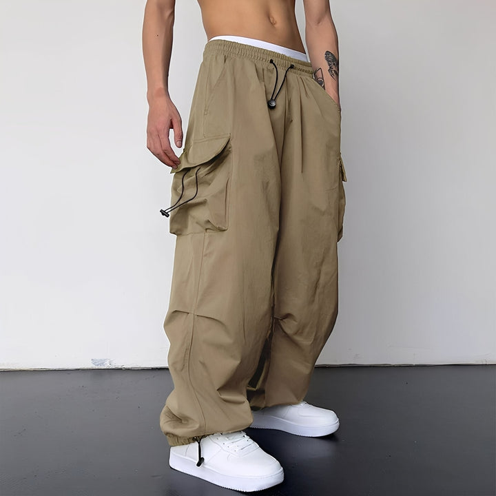 Pantalon baggy beige porté de trois quarts par un homme, avec baskets blanches 1