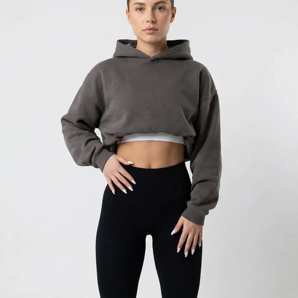 Buste d'une femme en legging noir taille haute et sweat à capuche court gris, mains posées sur les hanches. 6