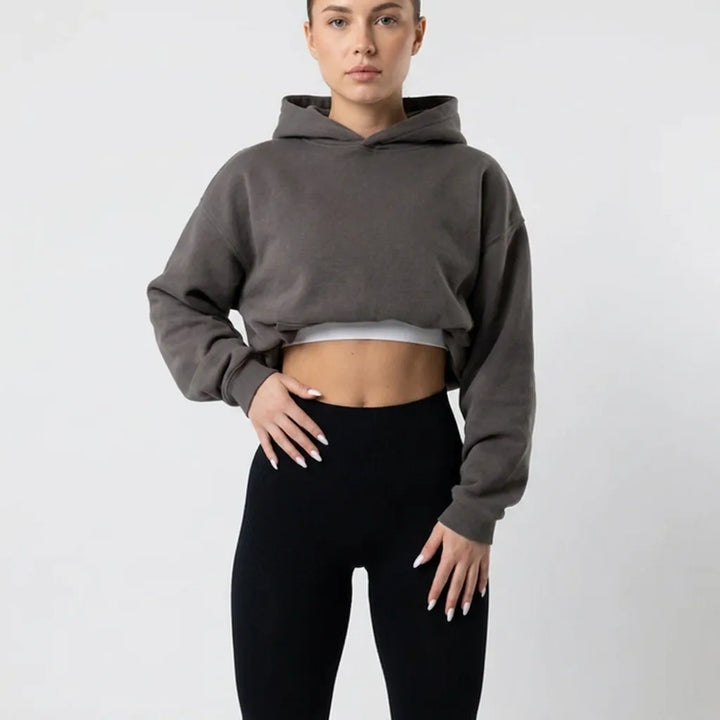 Buste d'une femme en legging noir taille haute et sweat à capuche court gris, mains posées sur les hanches. 6