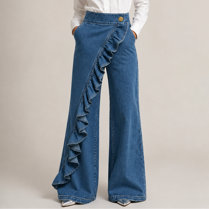 Vue de face en denim bleu moyen, portée avec chemise blanche et escarpins argentés, mains dans les poches, volant en diagonale. 1