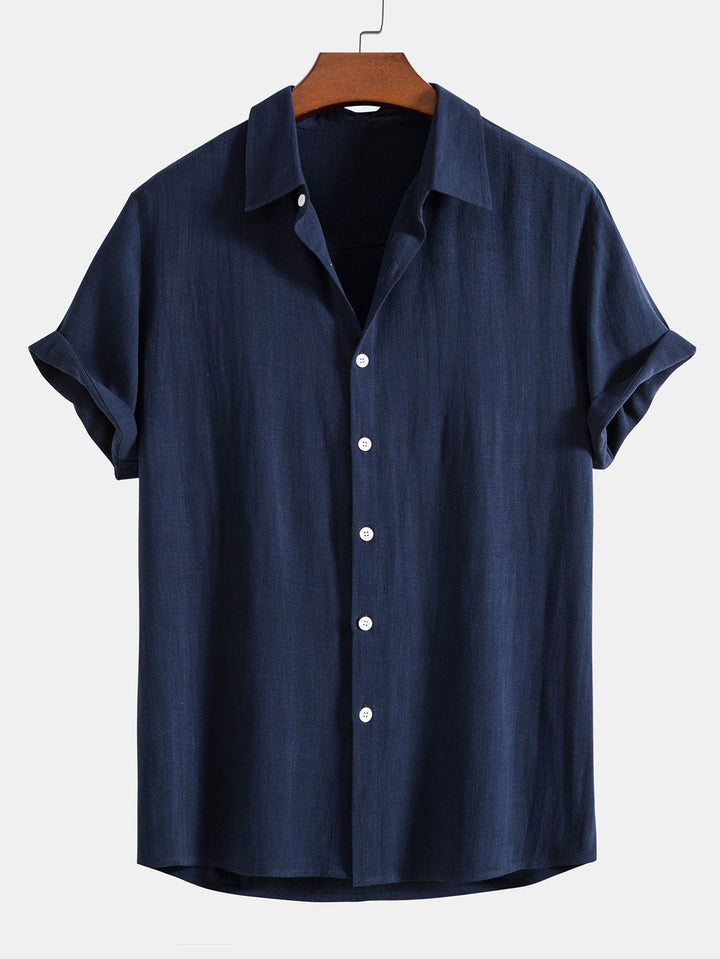 Chemise à manches courtes retroussées, coloris bleu marine, sur cintre en bois, vue de face avec boutons blancs. 4