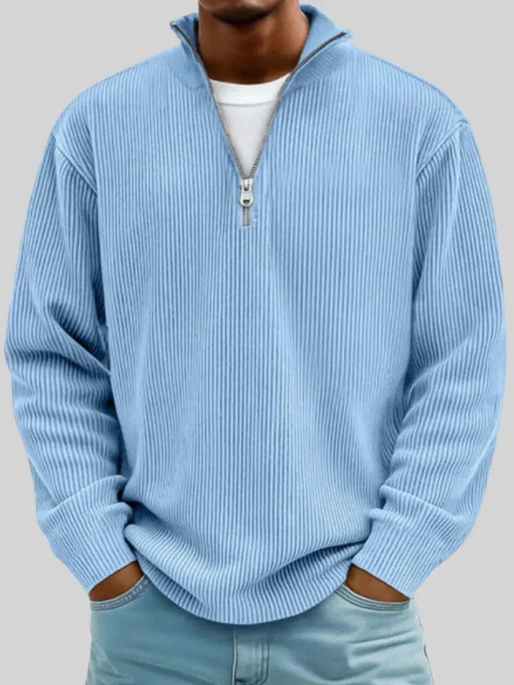 Homme portant le pull côtelé à col zippé en bleu ciel, mains dans les poches d'un jean, t-shirt blanc dessous. 1