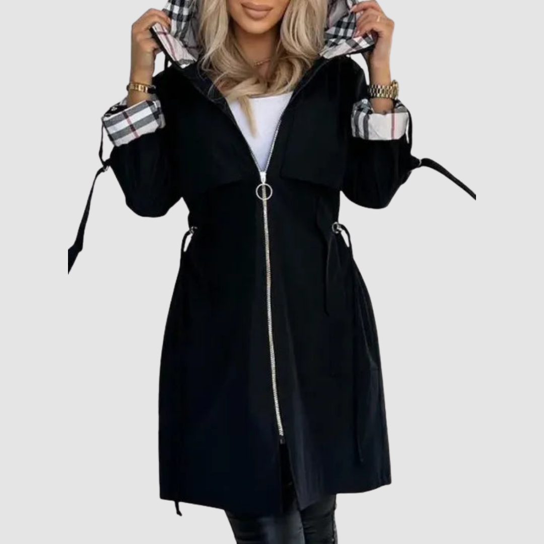 Femme portant le manteau noir zippé avec anneau métallique, capuche relevée laissant voir la doublure à carreaux, lanières aux manches. 3