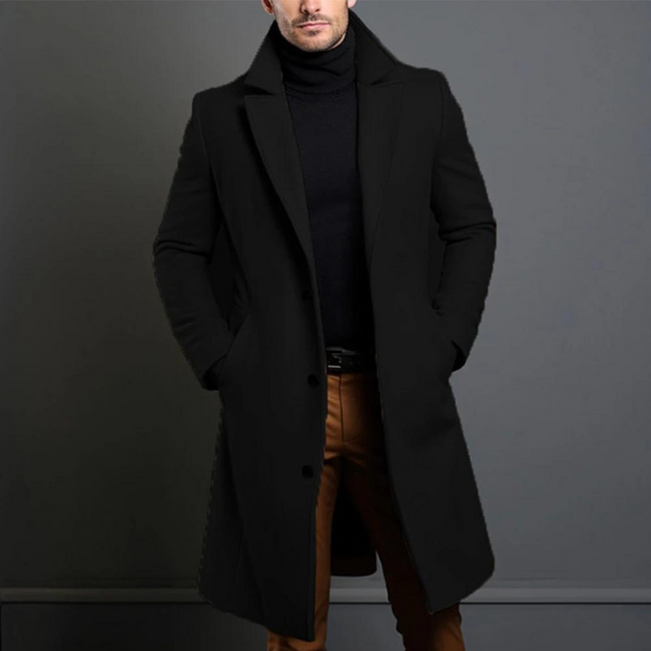 Homme portant le manteau long noir à col cranté et boutons, mains dans les poches, avec col roulé noir et pantalon marron. 1