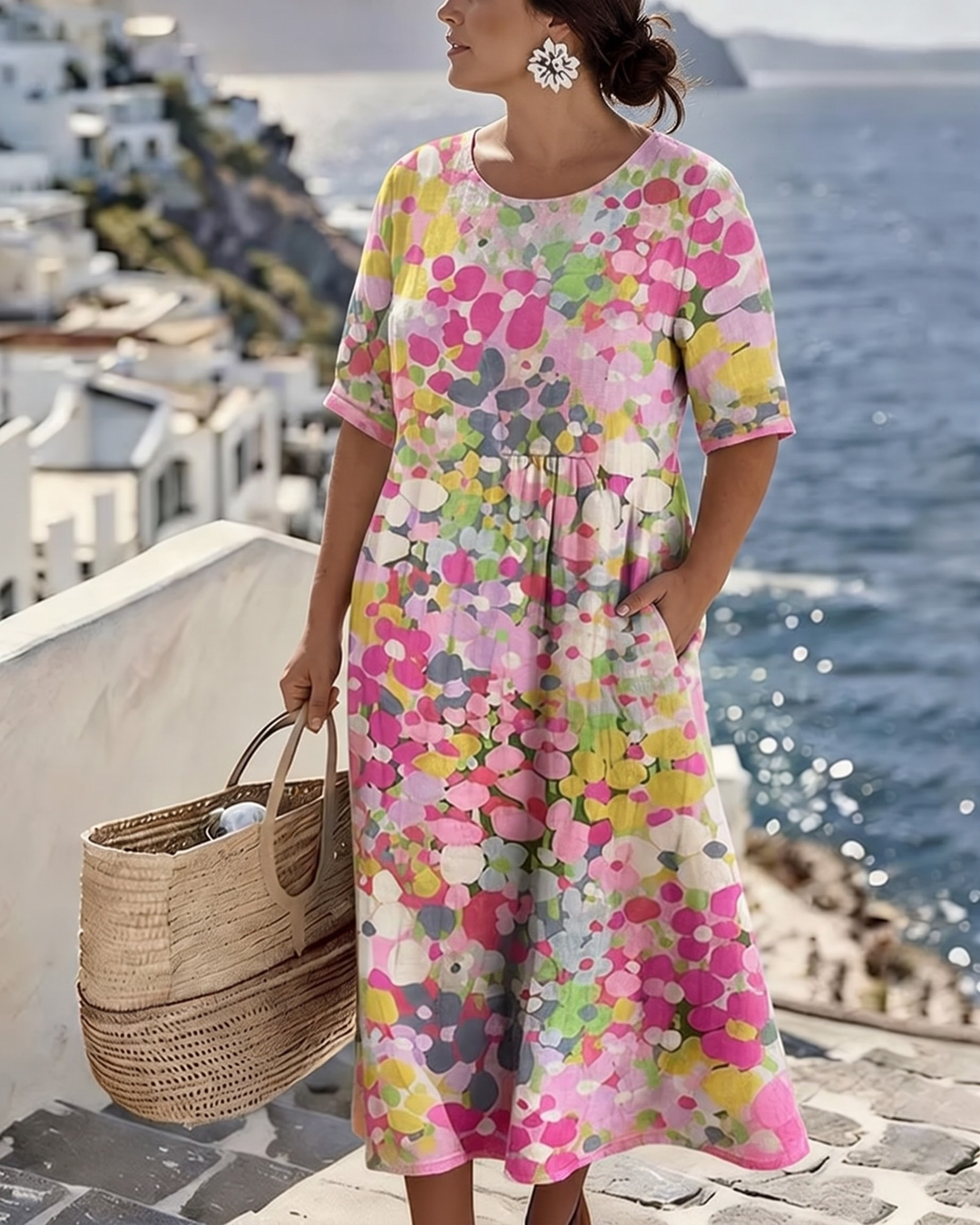 Robe florale rose et jaune portée par un mannequin en grande taille, main dans la poche, face à la mer 2