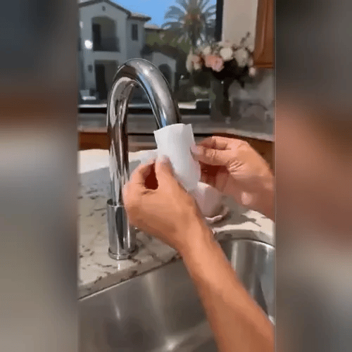 Mains installant un capuchon filtrant blanc sur le bec chromé d'un robinet de cuisine, au-dessus d'un évier en inox. 2