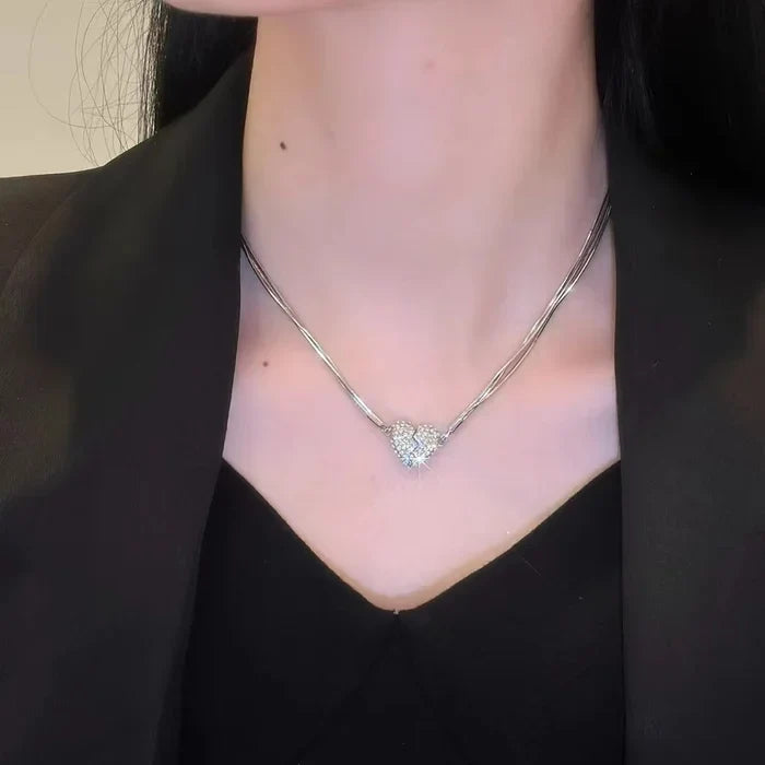 Collier à cœur scintillant en deux parties porté sur un haut noir à col en V, sous une veste noire. 6
