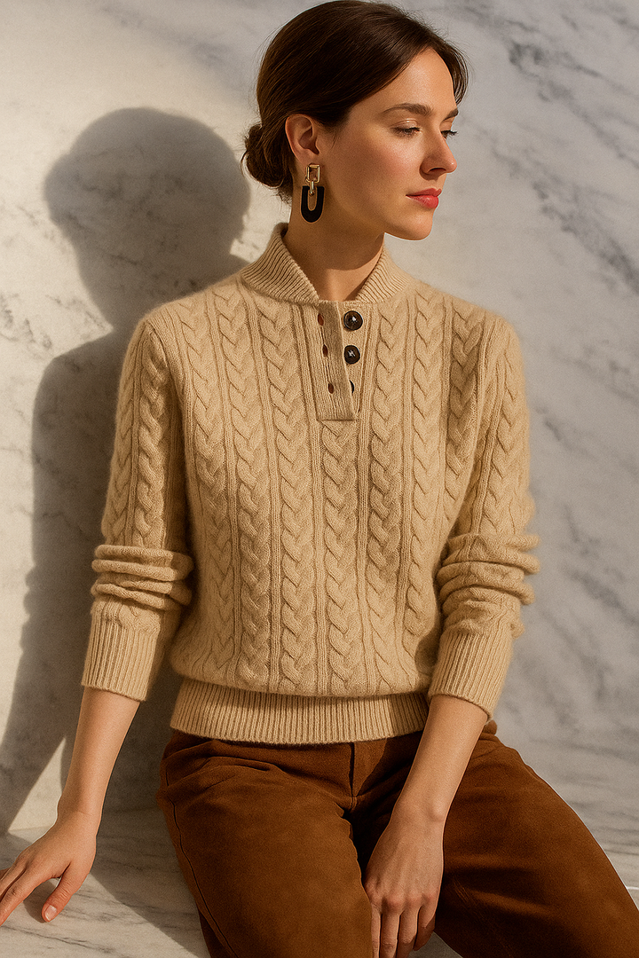 Femme portant le pull beige à torsades et col boutonné, assise devant un mur de marbre, avec un pantalon marron. 22